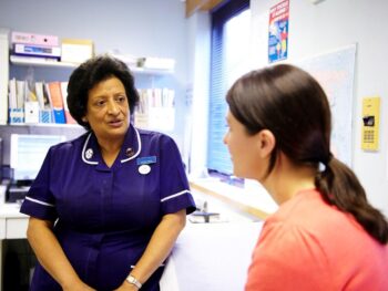 Photo of a female cancer patient sitting in a doctor's surgery and speaking with a Cancer Research UK nurse.