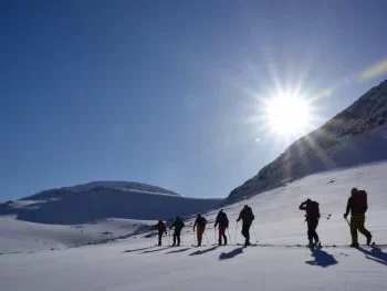 Six people walking across the snow as part of a ski sail Iceland expedition while the sun sets in the background