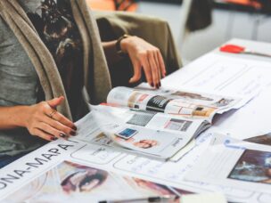 Picture of a woman reading news or preparing PR and press release plans with magazines spread out in front of her