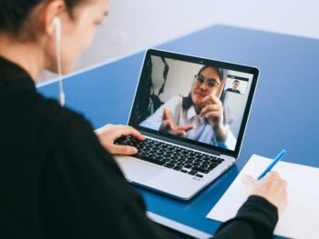 Photo of two women having a zoom meeting: one at the computer looking at the other on the screen. Photo by Anna Shvets from Pexels