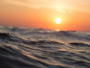 Dark blue rolling ocean in the foreground with an orange sky and the sun setting in the background. Photo by Sebastian Voortman from Pexels